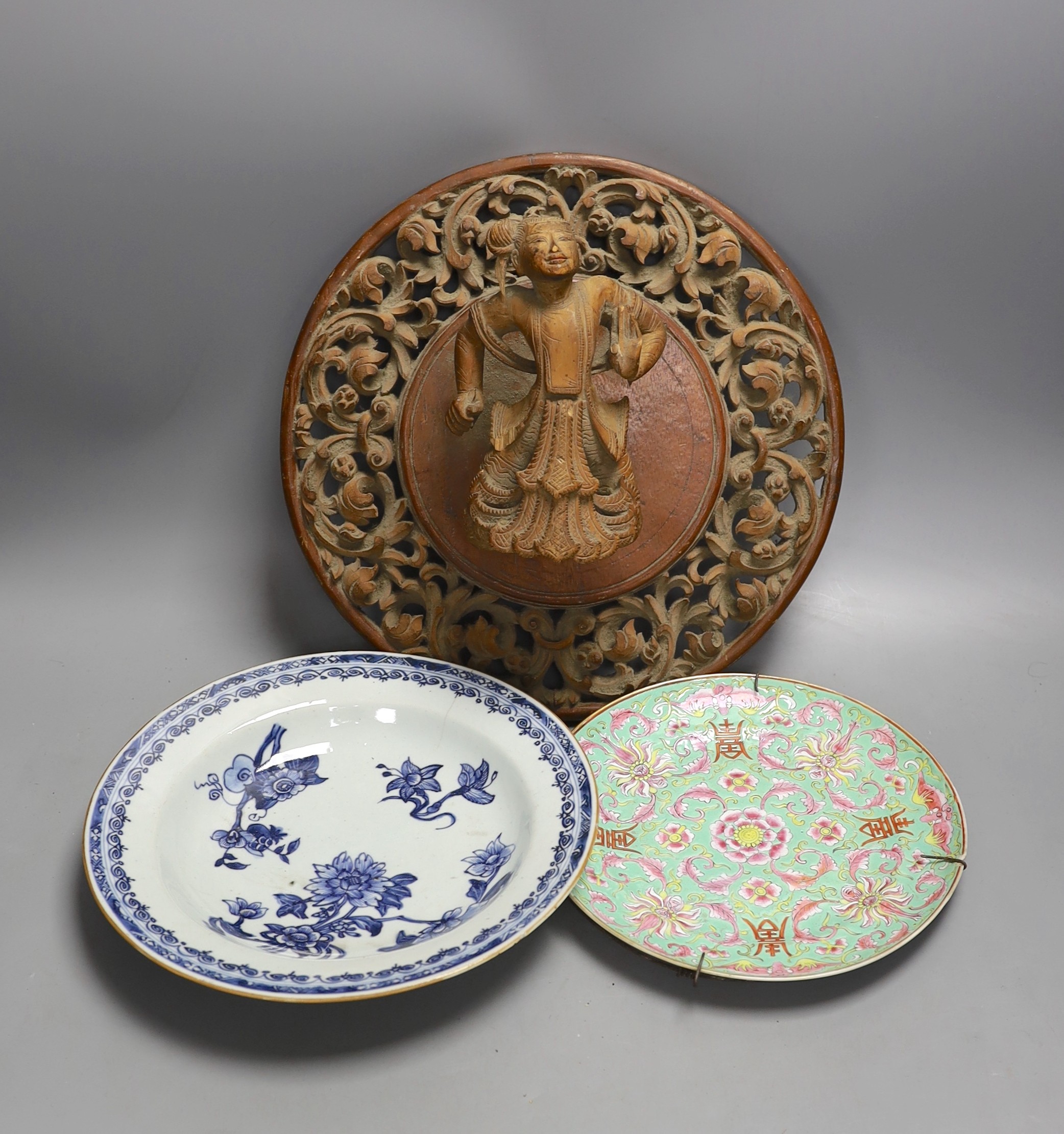 A Chinese blue and white plate with floral decoration, 23cm diameter, together with another plate and wooden panel relief of oriental figure (3)